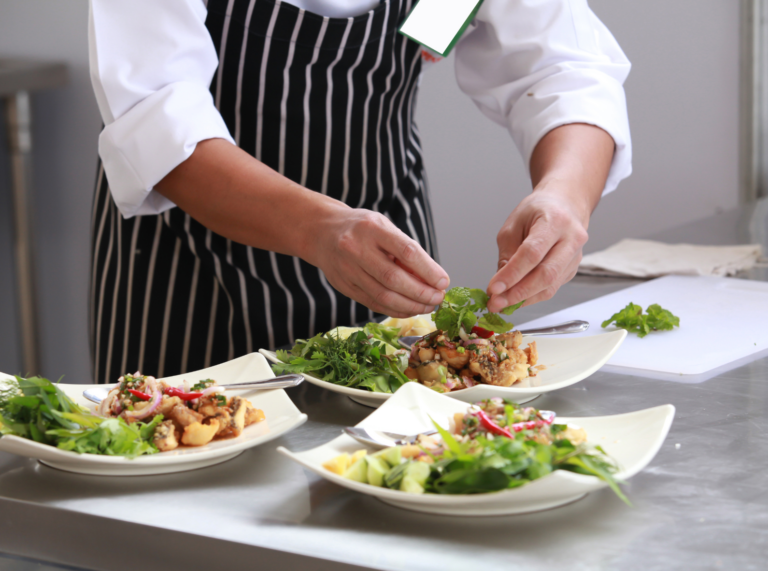 A chef carefully preparing several bowls of fresh salad in a restaurant kitchen, each bowl filled with vibrant greens, vegetables, and garnishes, showcasing the restaurant's commitment to fresh, healthy ingredients.