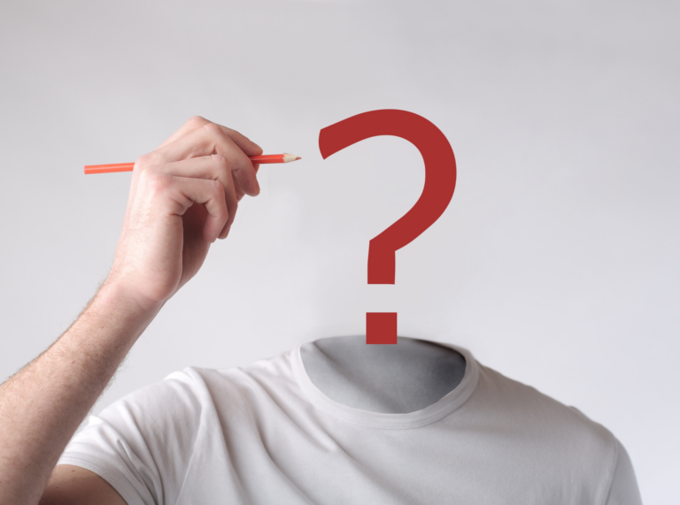 An image of a person wearing a white t-shirt with no visible head, replaced by a red question mark. A hand is holding a red pencil, appearing to draw the top of the question mark, symbolizing uncertainty or seeking identity.