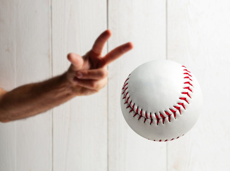 A close-up image of a hand in motion, pitching a baseball. The baseball, with its red stitching, is in focus mid-air, while the hand and background are slightly blurred to emphasize the action of the pitch.