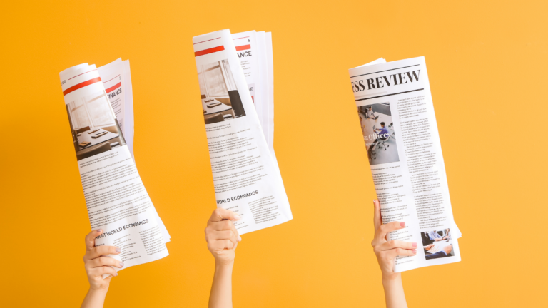 Three hands holding up rolled newspapers against a bright orange background. This image highlights enthusiastic media coverage.