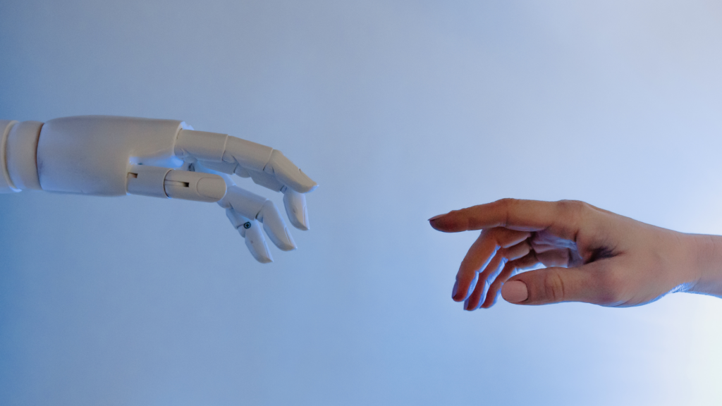 An artistic image showing a robotic hand and a human hand reaching toward each other, symbolizing the connection between technology and humanity, set against a gradient blue background.