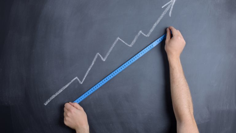 Chalkboard with a graph pointed upwards. Two hands stretch out a tape measurer to measure the graph. This image hints at measuring your public relations wins.